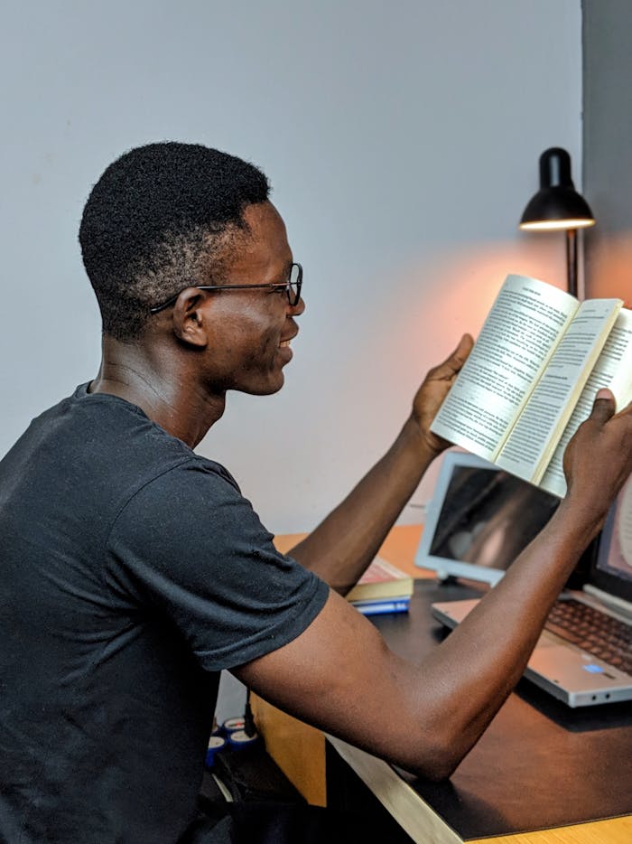 African man engaged in reading at a study desk, illuminated by a lamp.